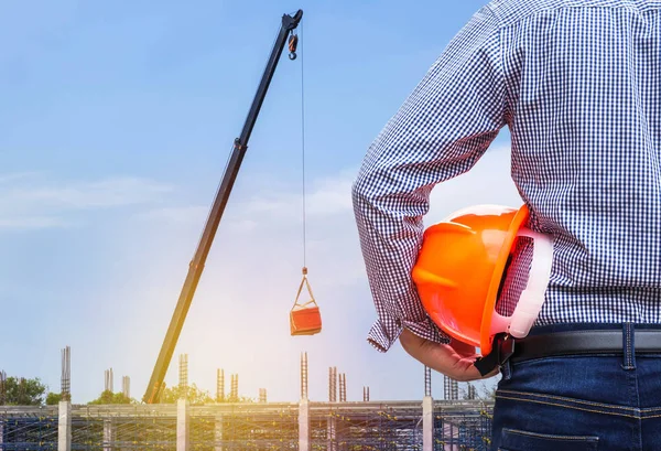 engineer holding yellow safety helmet in building construction site with crane