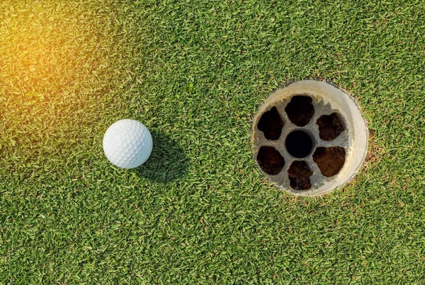 Белый мяч для гольфа возле лунки на зеленой траве — стоковое фото