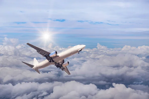 Avión comercial blanco volando hacia el cielo a gran altitud por encima de las nubes blancas con luz solar — Foto de Stock