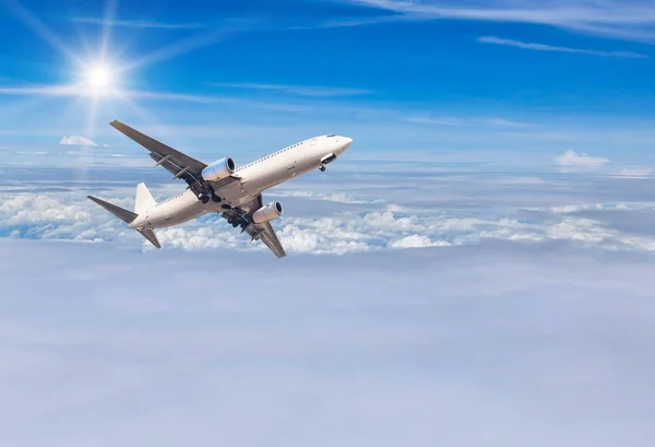 White commercial airplane flying away in to sky high altitude above the white clouds with sunlight — Stock Photo, Image