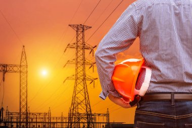 sarı güvenlik kask ile yüksek gerilim elektrik pilon ayağı elektrik santraller trafo günbatımı üzerinde tutan mühendisi 