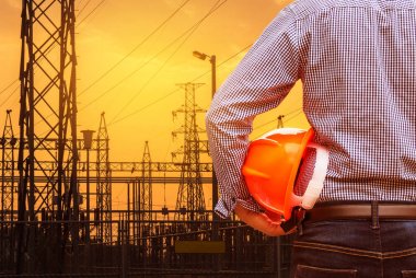 Sarı güvenlik kask yüksek gerilim elektrik pilon ayağı ile elektrik santraller Trafo Merkezi günbatımı arka planda tutan mühendisi  