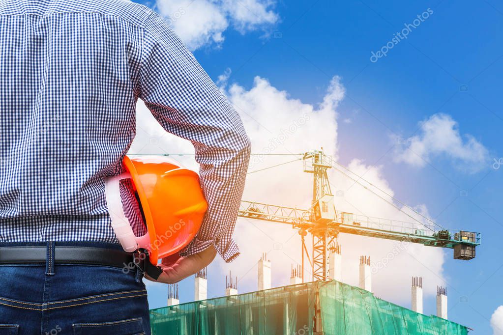 engineer holding yellow safety helmet in building construction site with crane