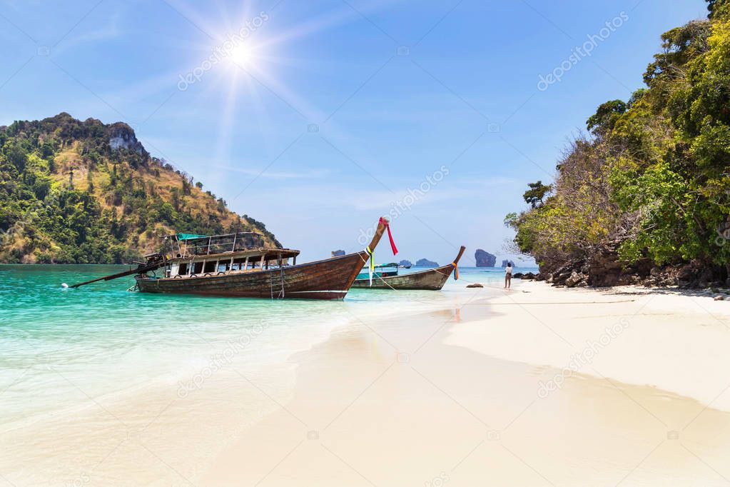 longtail boats mooring on the beach between small limestone islands in andaman sea at Krabi, Thailand with blue sky.