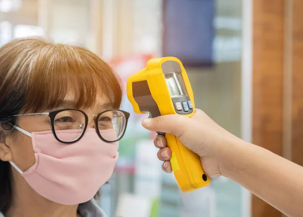 Dijital tıbbi elektronik termometre kullanan güvenlik görevlisi vücut ısısını ölçüyor Asyalı yolcuları koruyor. Koronavirüs COVID-19 'un havaalanına girmeden önce bulaşıcı hastalıkların yayılmasını önlüyor.
