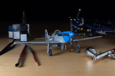 Uçak ve ölçek figürleri, aletlerle hobi modellik setini temsil ediyor. P-51 modeli, fırçalar, boya ve hava fırçası..