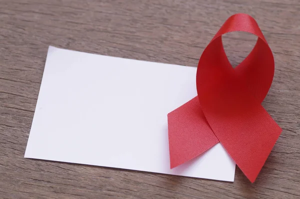 Красная лента и белая пустая бумага на деревянном фоне, знак СПИДа с копировальным местом — стоковое фото