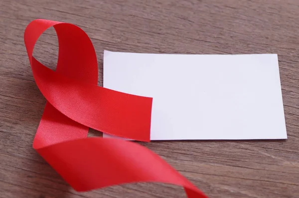 AIDS, красная лента и белая бумага слово в слово, чтобы помочь и защитить, на деревянном фоне — стоковое фото