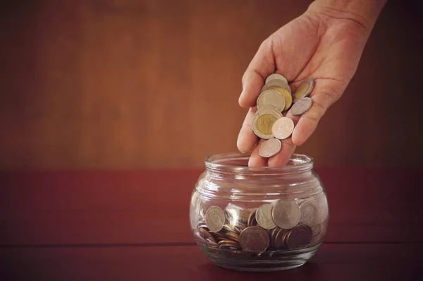 Hand put coins in jar on dark wood table, concept in save and investment in business — Stock Photo, Image