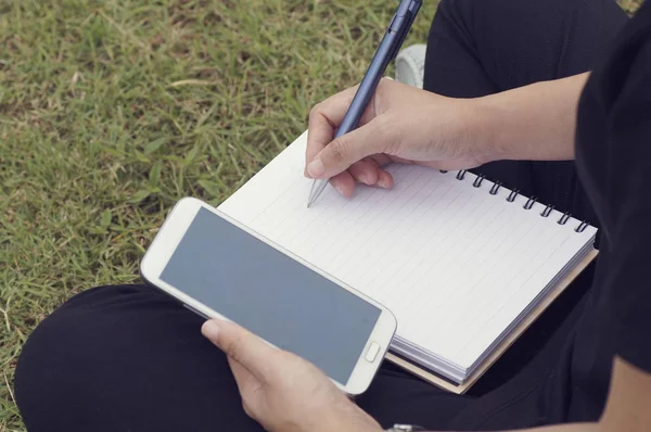 Ręka kobiety pisanie na papierze i używać telefon w złożony — Zdjęcie stockowe