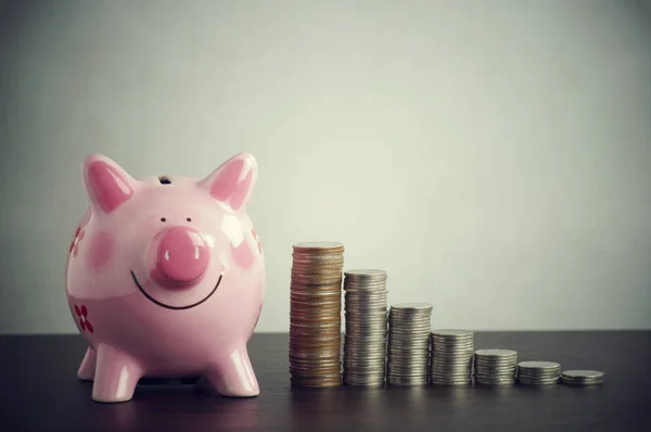 Pila de monedas de dinero con alcancía rosa en la mesa de madera — Foto de Stock