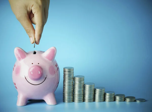 Hand put money on pink of piggy bank and  pile of coins on blue — Stock Photo, Image