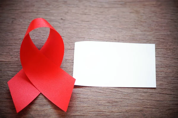 AIDS, красная лента и белая бумага слово в слово, чтобы помочь и защитить, на деревянном фоне — стоковое фото