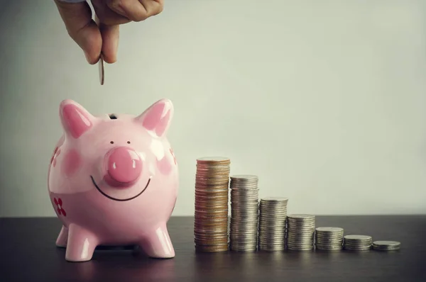 お金を入れる貯金箱と青い背景上のコインの山のピンクの手 — ストック写真