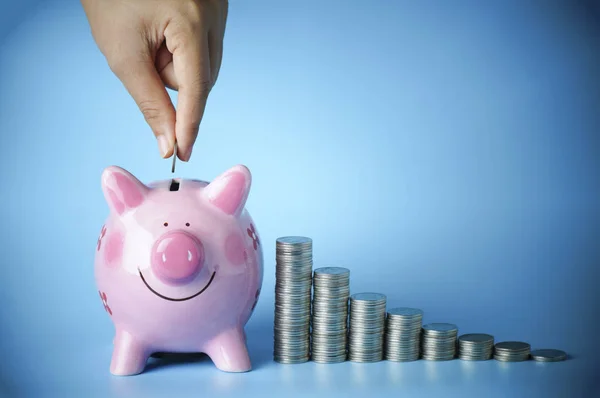 Hand put money on pink of piggy bank and  pile of coins on blue background — Stock Photo, Image