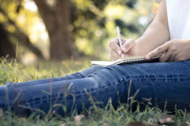 genç kadın yazma not defterinde park, kavramı eğitim ve bilgi kapatın