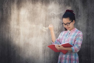 Asyalı kadın vardır sevindim ve okuma kitabı karanlık çimento duvar arka plan üzerinde eğitim, başarı veya Son'u eğitim ve bilgi kavramı, Beautiful Genç.