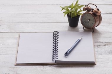 Not kağıdı, kitap ve kalem ile çalar saat, ahşap masa üzerinde bitki