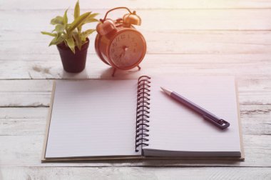 Not kağıdı, kitap ve kalem ile çalar saat, ahşap masa üzerinde bitki