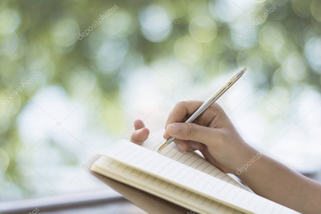 Hand writing of women on note paper on  balcony and green bokeh of tree background in morning