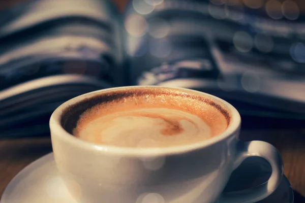 Taza de café con revista en la mesa en la cafetería en tono oscuro y vi — Foto de Stock