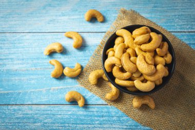 Kavrulmuş kaju fıstığının üst görüntüsü siyah kasede tuz içinde yumuşak mavi eski ahşap masada.