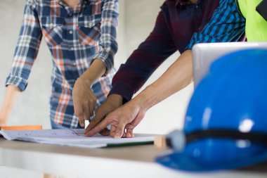 Mühendislerden oluşan bir ekip mavi baskı üzerine plan yapacak ve çalışma masasındaki inşaat tasarımı hakkında tartışacaklar.  