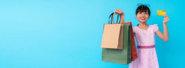 Mutlu Asyalı genç kız alışveriş çantası tutuyor. Stüdyoda mavi afiş üzerinde kredi kartı var. Moda tarzı için para ödenen bir yaşam tarzı.