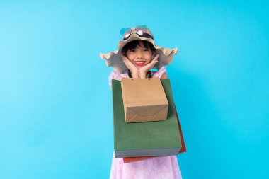 Stüdyoda mavi arka planda alışveriş çantası taşıyan mutlu Asyalı genç kız stili. Moda tarzı için para ödenen bir yaşam tarzı.