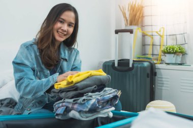 Tatil konsepti için hazırlık ve seyahat planı, Taylandlı ve Asyalı mutlu kadın valizlere bavul doldurup yatağa gitmek için hazırlanıyor.