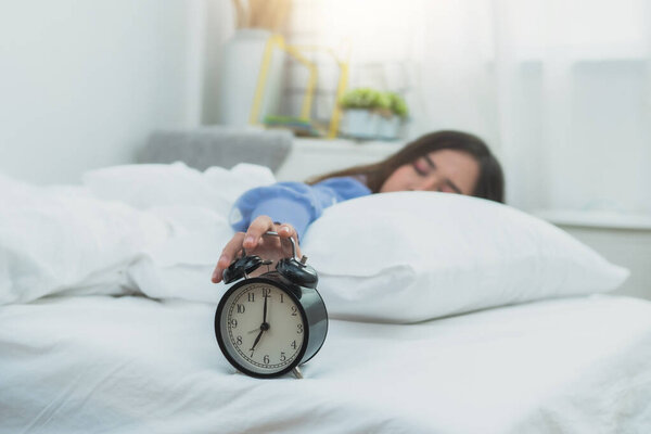 Woman's hand touch alarm clock on bed, lazy and rest time on holiday concept