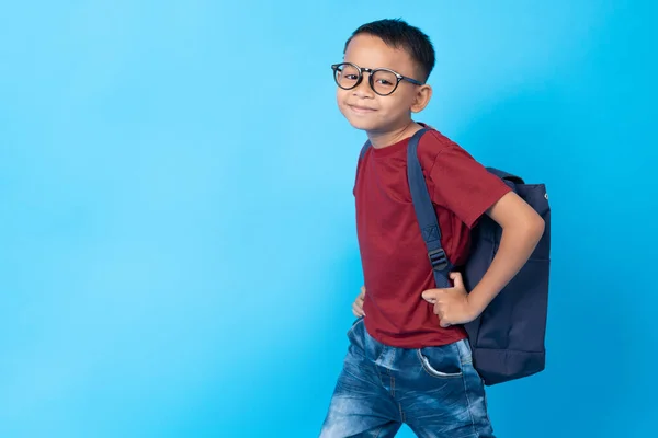 Little Asia boy student in red shirt with school bag on blue background in studio