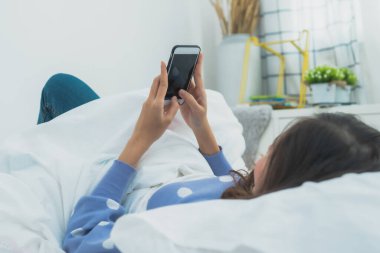 Kadın yatakta telefon kullanıyor, rahatlıyor ve yatak odasında internette sörf yapıyor.