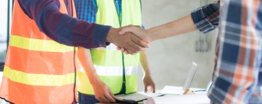 İki iş adamının tokalaşması, mimarlık yaptıktan ve plan yapıldıktan sonra, mühendislik objeleri iş yerinde