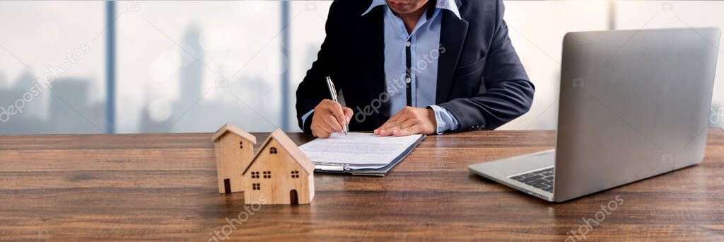 real estate, property and home owner signing contract by bank agency concept, small wooden house model on office table with signing on rental agreement paper to rent above mentioned residence