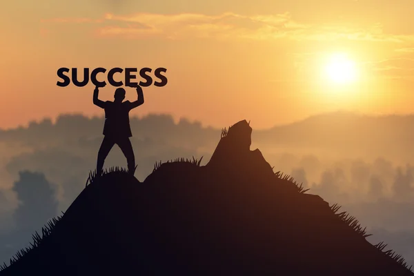 Silhouette Man Holds a sign of success on mountain top over sky — Stock Photo, Image