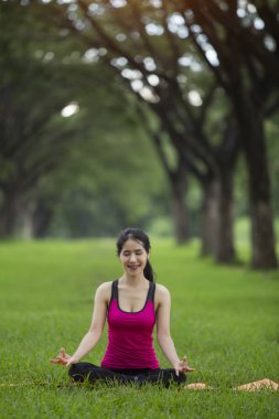 Genç kadın parkta yoga yapıyor.