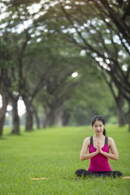 Genç kadın parkta yoga yapıyor.