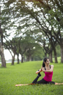 Genç kadın parkta yoga yapıyor.