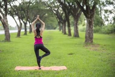Genç kadın parkta yoga yapıyor.