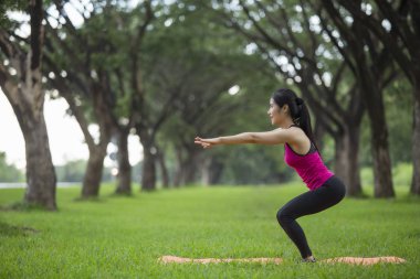 Genç kadın parkta yoga yapıyor.