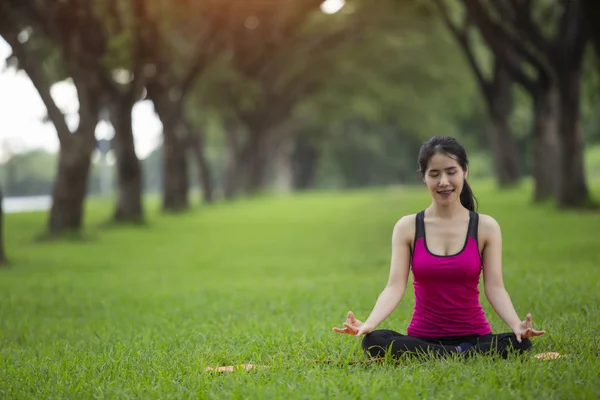 Genç kadın parkta yoga yapıyor.