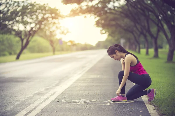 Mujer joven corredora atando cordones en carretera rural — Foto de Stock