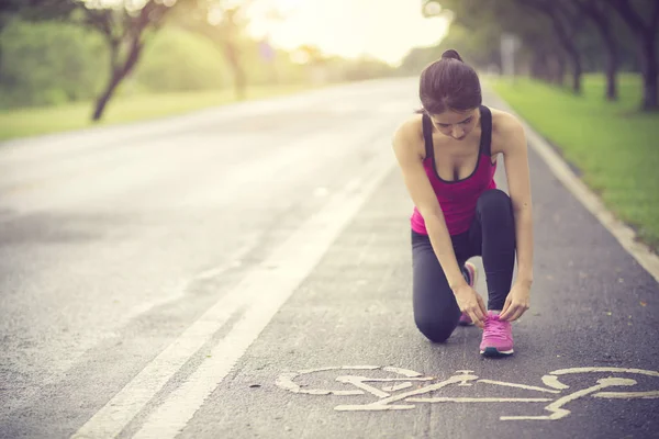 Молода жінка бігун зав'язує шнурки на сільській дорозі — стокове фото