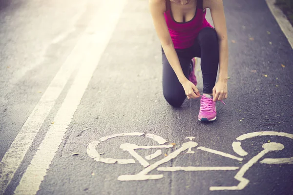 Mujer joven corredora atando cordones en carretera rural — Foto de Stock