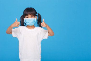 Little asian girl wearing mask for protect pm2.5 and show thumbs up gesture for good air outdoor.Air pollution pm2.5 and Coronavirus concept clipart
