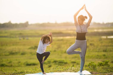 Parkta güneşli ışıkta yoga yapan iki tatlı kız..