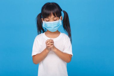 PM2.5 ve Coronavirus Covid-19 'u korumak için maske takan Asyalı bir kız. Pazar günü GodD.Online kilisesine dua etmek için evde kal. Küçük Asyalı kız evde dua ediyor. Sosyal uzaklık. Mavi arka planda.