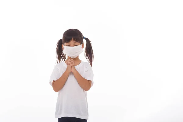 Asian girl wearing mask for protect pm2.5 and coronavirus Covid-19.Stay at home praying to GOD.Online church worship in sunday.Little asian girl hand praying at home.Social distancing.on white background