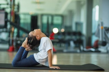 Küçük tatlı kız yoga yapıyor. Paspasın üstünde duruyor.